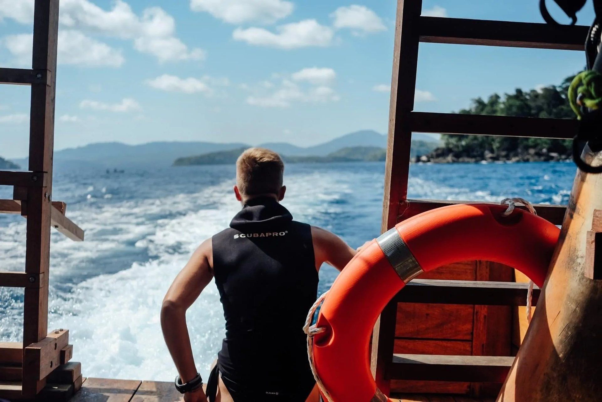 A diver at the stern watching the boat’s wake, with the hills of Pulau Weh on the horizon