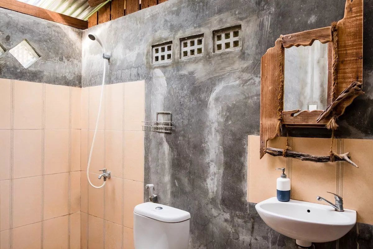 The bathroom of the Fancy Bungalow, with an open shower, a washbasin and a driftwood-framed mirror.