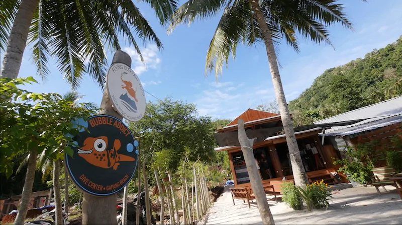 The Bubble Addict Dive Center sign among palm trees at the entrance to the shop on Gapang Beach